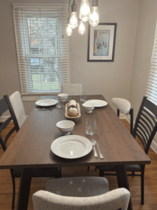 Dining room with a modern wood table set for six, soft lighting, and a large window at Rosslyn Retreat.