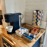 Coffee bar with a Keurig machine, K-cup selection, creamers, and a basket of snacks at Rosslyn Retreat.